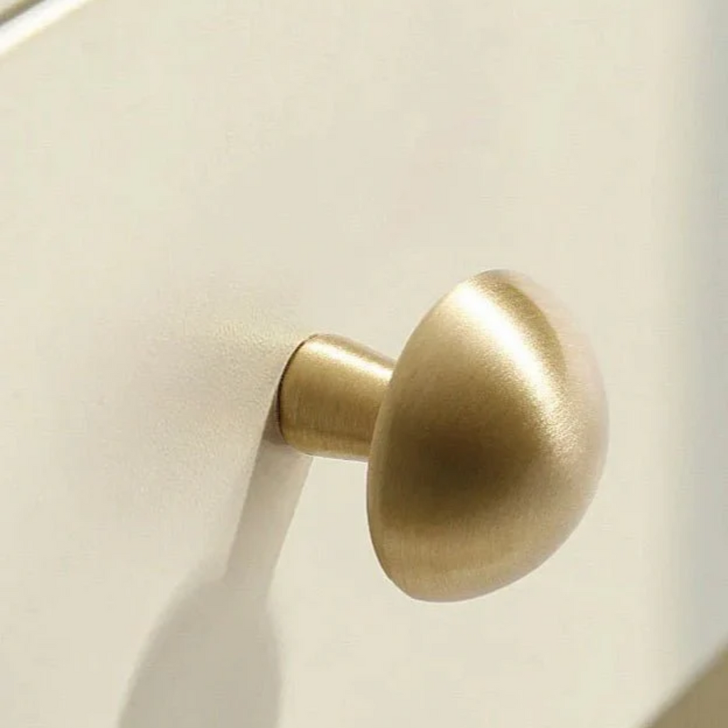Brass Essence mushroom-shaped solid brass cabinet knob with a polished finish, mounted on a wooden cabinet door.