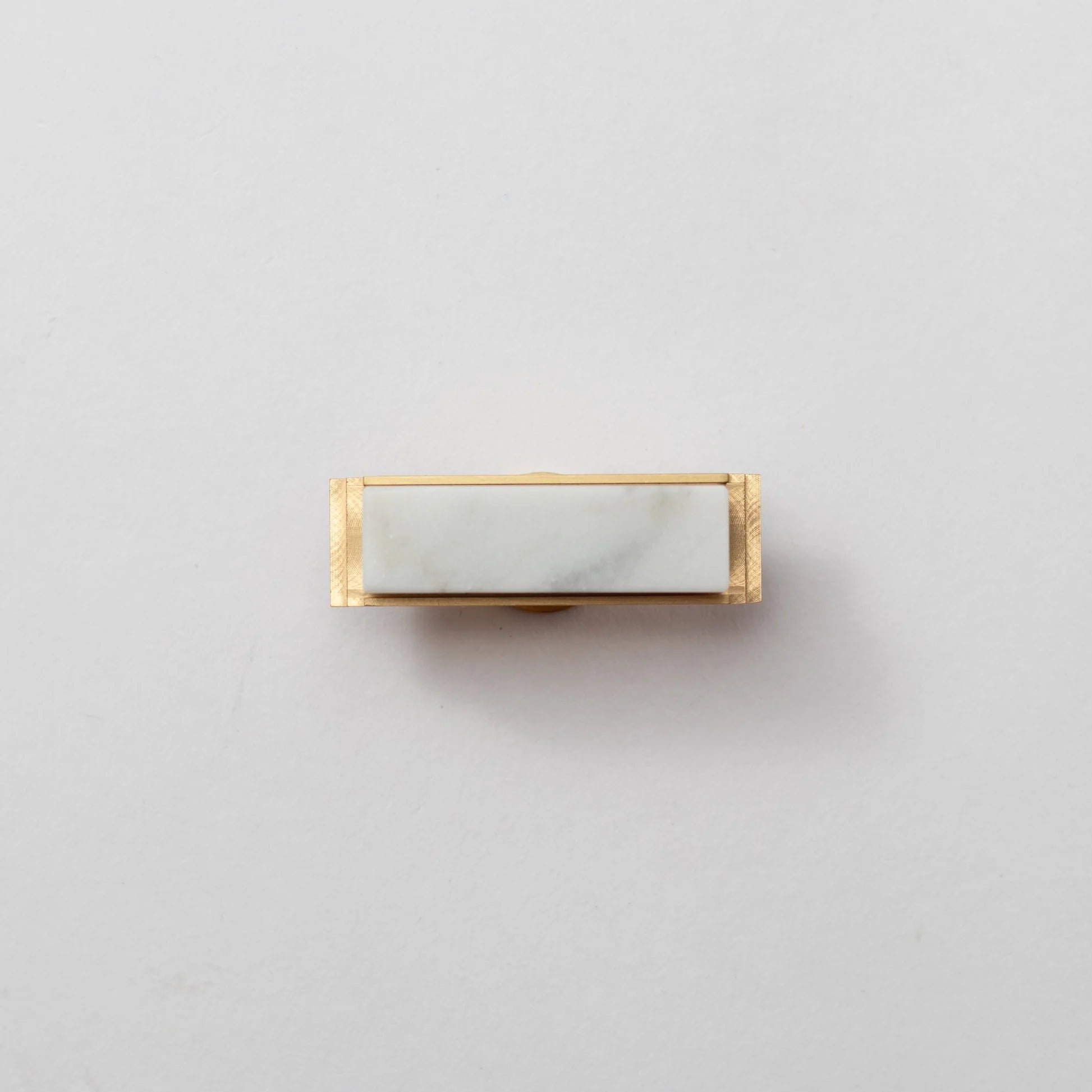 Modern white marble and brass T-bar handle by Brass Essence, shown on a sleek furniture piece.